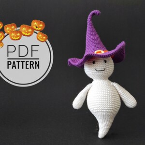 Könnte beinhalten: Ein weißer gehäkelter Geist, der einen lila Hexenhut mit einer orangefarbenen Schnalle trägt. Der Geist hat ein lächelndes Gesicht und steht auf einem schwarzen Hintergrund.  PDF PATTERN.