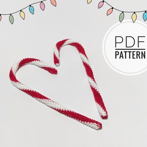 May include: Two handmade crochet candy canes with red and white stripes, arranged on a white surface. The image includes a string of colorful lights and the text "PDF PATTERN" in a circular design, suggesting a holiday craft project.
