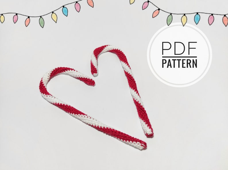 May include: Two handmade crochet candy canes with red and white stripes, arranged on a white surface. The image includes a string of colorful lights and the text "PDF PATTERN" in a circular design, suggesting a holiday craft project.
