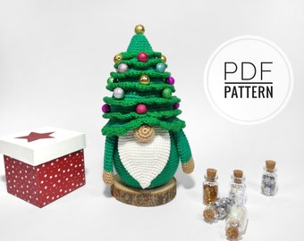 Puede incluir: Un gnomo de árbol de Navidad de crochet verde con barba blanca y base de madera. El gnomo lleva un gorro verde con adornos coloridos. La imagen también incluye una caja roja con estrellas blancas y un cartel que dice "PDF PATTERN".