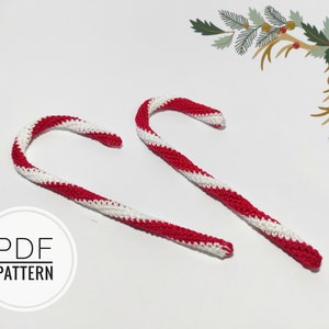 May include: Two handmade crochet candy canes with red and white stripes. The candy canes are curved and have a textured appearance. The image also includes a decorative floral element and the text "PDF PATTERN".