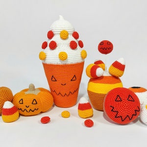 May include: A collection of crocheted Halloween decorations, including pumpkins, candy corn, and an eye. The decorations are all orange, yellow, and white.