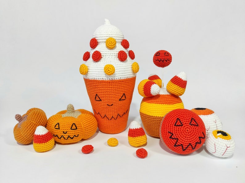 May include: A collection of crocheted Halloween decorations, including pumpkins, candy corn, and an eye. The decorations are all orange, yellow, and white.