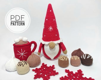 May include: A red crocheted gnome with a white beard and a red hat with a white snowflake. The gnome is surrounded by crocheted chocolate candies, a red mug with marshmallows, and two red crocheted snowflakes.