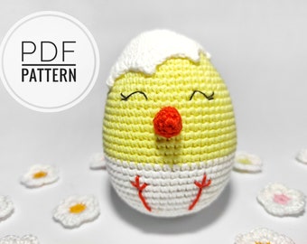 May include: A crocheted chick amigurumi toy with a yellow body, white shell, and red beak. The chick has black eyes and a white background.
