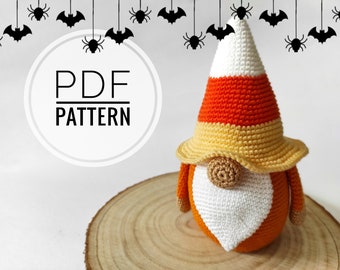 May include: Crochet pattern for a candy corn gnome with a white beard, orange body, and yellow hat. The pattern is available as a PDF download. The image also includes black bats and spiders hanging from strings.