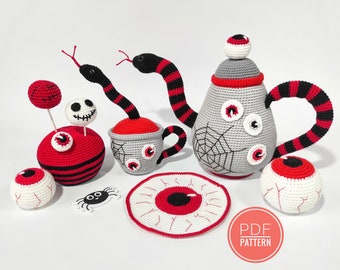 May include: A crocheted Halloween tea set featuring a teapot, cup, saucer, and eyeball decorations. The teapot has a spiderweb design and a black and red striped handle. The cup has a red rim and a white base with a spiderweb design. The saucer has a red eyeball design. The set also includes a crocheted eyeball, a crocheted spider, and a crocheted lollipop with an eyeball on top. The text "PDF PATTERN" is visible in the image.