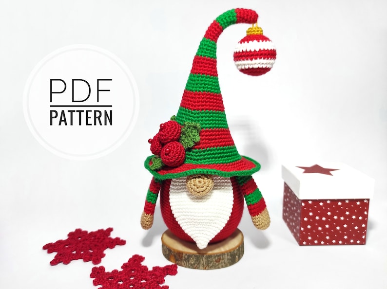 May include: A handmade Christmas gnome with a red body, white beard, and a green and red striped hat. The gnome holds a red and white striped ornament. The image also includes a gift box and red snowflake decorations. The text "PDF PATTERN" is in a circle.