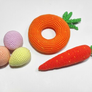 Puede incluir: Un conjunto de juguetes de crochet que incluye una zanahoria, un anillo y tres huevos peque&ntilde;os en tonos rosa, melocot&oacute;n y amarillo.