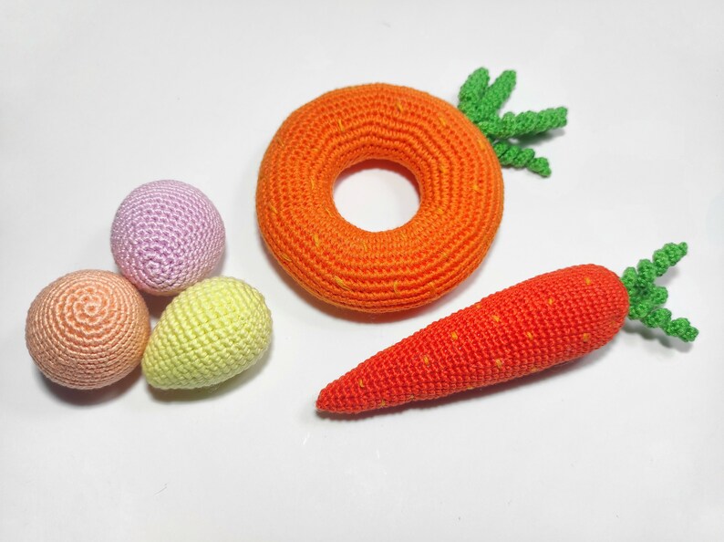 Puede incluir: Un conjunto de juguetes de crochet que incluye una zanahoria, un anillo y tres huevos peque&ntilde;os en tonos rosa, melocot&oacute;n y amarillo.