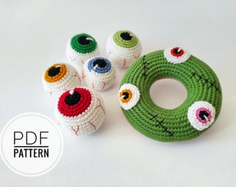 Könnte beinhalten: Eine Sammlung gehäkelter Halloween-Dekorationen, darunter mehrere augenförmige Ornamente mit roten, gelben, grünen und blauen Iris. Ein grüner gehäkelter Kranz mit Nahtdetails und drei Augenschmuck ist ebenfalls vorhanden. Der Text "PDF PATTERN" ist enthalten.