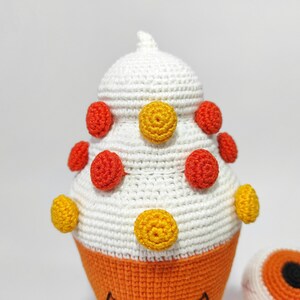 May include: A white crocheted cone-shaped toy with orange and yellow polka dots. The toy has a small orange eye on the side.
