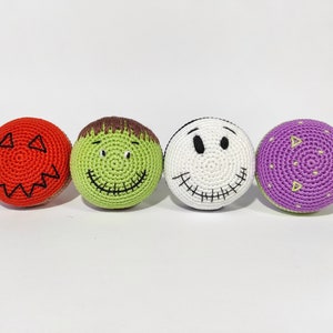 May include: Four crocheted Halloween-themed balls. One is red with a jack-o'-lantern face, one is green with a Frankenstein face, one is white with a stitched-up smile, and one is purple with a dotted pattern.