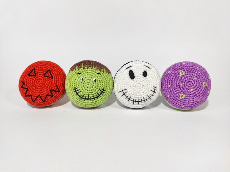 May include: Four crocheted Halloween-themed balls. One is red with a jack-o'-lantern face, one is green with a Frankenstein face, one is white with a stitched-up smile, and one is purple with a dotted pattern.