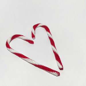 May include: Two handmade crochet candy canes in red and white stripes, arranged in a heart shape. These festive decorations are perfect for Christmas or holiday-themed decor. The candy canes are made with a textured stitch.