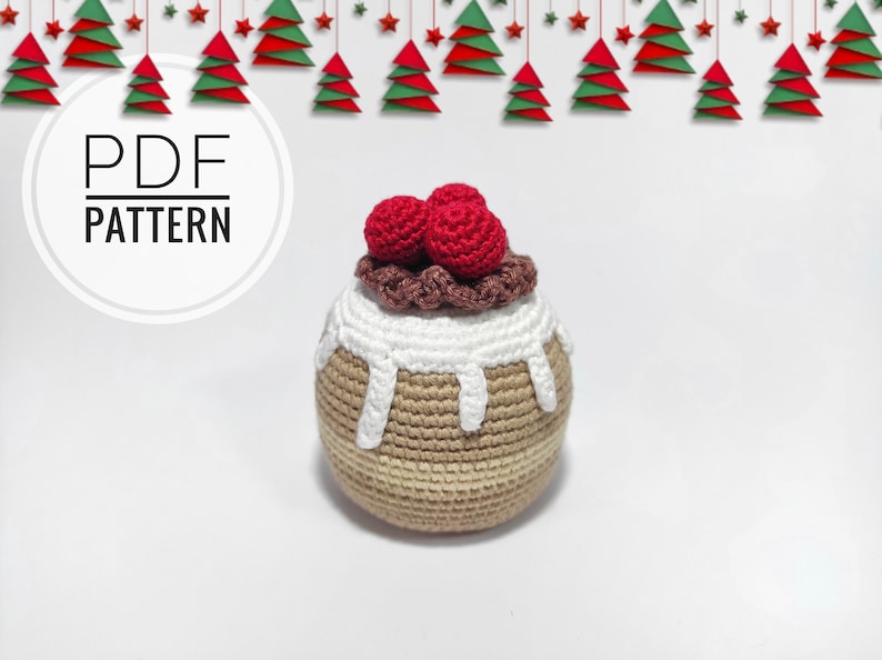 May include: Crochet pattern for a Christmas pudding ornament. The ornament is brown and beige with white icing and red cherries on top. The pattern is available as a PDF download.