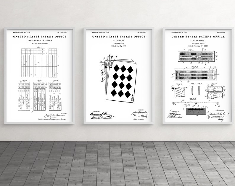 May include: Three framed patent prints. The prints are black and white, featuring detailed diagrams and text. The central print showcases a playing card design. The other two prints display technical drawings. The frames are white, and the background is a wooden floor.