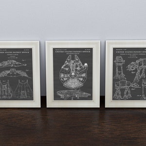 May include: Three framed prints of vintage patent drawings for Star Wars vehicles. The left print shows a TIE fighter, the middle print shows the Millennium Falcon, and the right print shows an AT-AT walker.