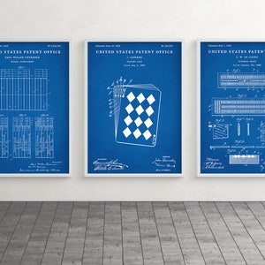 May include: Three framed patent prints with white frames. The prints feature white technical drawings on a blue background. The prints include text from the United States Patent Office. One print shows a playing card design.