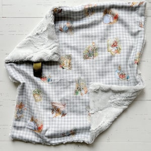 May include: A gray and white gingham baby blanket with a Peter Rabbit print. The blanket is soft and cuddly, perfect for a baby's nursery.