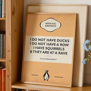 May include: A framed rectangular poster with a tan background featuring the text SPECIAL EDITION, I DO NOT HAVE DUCKS, I DO NOT HAVE A ROW, I HAVE SQUIRRELS & THEY ARE AT A RAVE, AN AUTOBIOGRAPHY, COMPLETE, and UNABRIDGED with a small penguin icon.