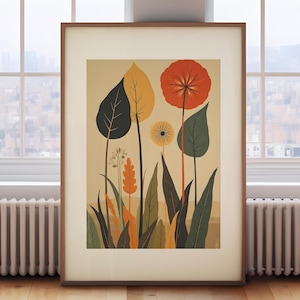 May include: A framed botanical print featuring stylized flowers and foliage in shades of orange, yellow, green, and black against a beige background. The artwork is displayed on a wooden floor near a window, creating a natural aesthetic.