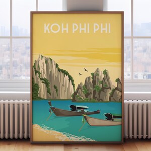 May include: A framed travel poster with the text "KOH PHI PHI" in a vintage style. The poster depicts a tropical scene with boats on turquoise water, rocky islands, and a yellow sky. The poster is displayed on a wooden floor.
