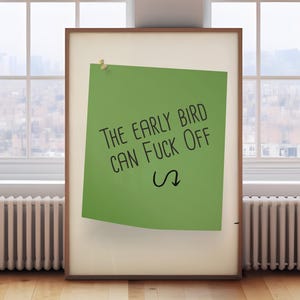 May include: A framed poster featuring a green sticky note with the text "THE EARLY BIRD CAN FUCK OFF" in black, and a curved arrow. The poster is in a room with a window and a radiator, on a wooden floor.