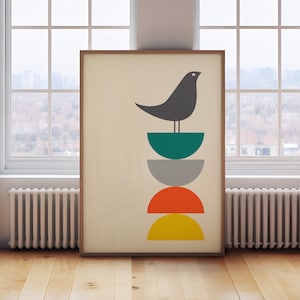 May include: A framed wall art print featuring a dark gray bird perched atop a vertical stack of four semi-circles in teal, gray, orange, and yellow. The design is set against a light cream background, enclosed within a simple wooden frame.