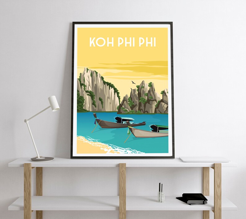 May include: A framed art print featuring a tropical beach scene with the text "KOH PHI PHI" at the top. The artwork depicts turquoise water, sandy beaches, and traditional longtail boats. Towering rock formations and a yellow sky complete the scene.