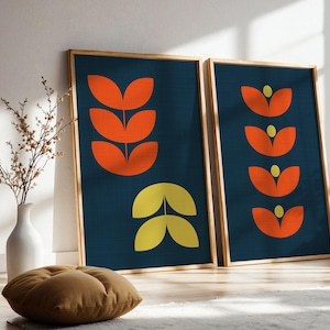 May include: Two rectangular framed wall art prints featuring a dark blue background with orange and yellow leaf-like shapes. The left print displays a vertical stack of three orange leaves above two yellow leaves. The right print shows four orange petals.