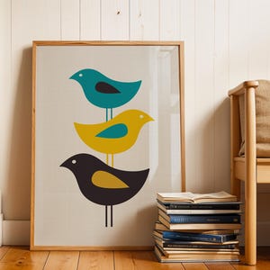 K&ouml;nnte beinhalten: Ein gerahmter Kunstdruck mit drei vertikal gestapelten, stilisierten V&ouml;geln auf hellgrauem Hintergrund. Der oberste Vogel ist blaugr&uuml;n, der mittlere gelb und der untere dunkelgrau. Jeder Vogel hat einen kontrastierenden Fl&uuml;gel und ein wei&szlig;es Auge.
