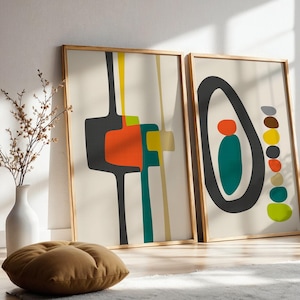 May include: Two framed rectangular wall art prints featuring abstract shapes in charcoal, orange, yellow, and teal on a cream background. The left print displays geometric lines and blocks, while the right print shows a large oval with stacked circles.