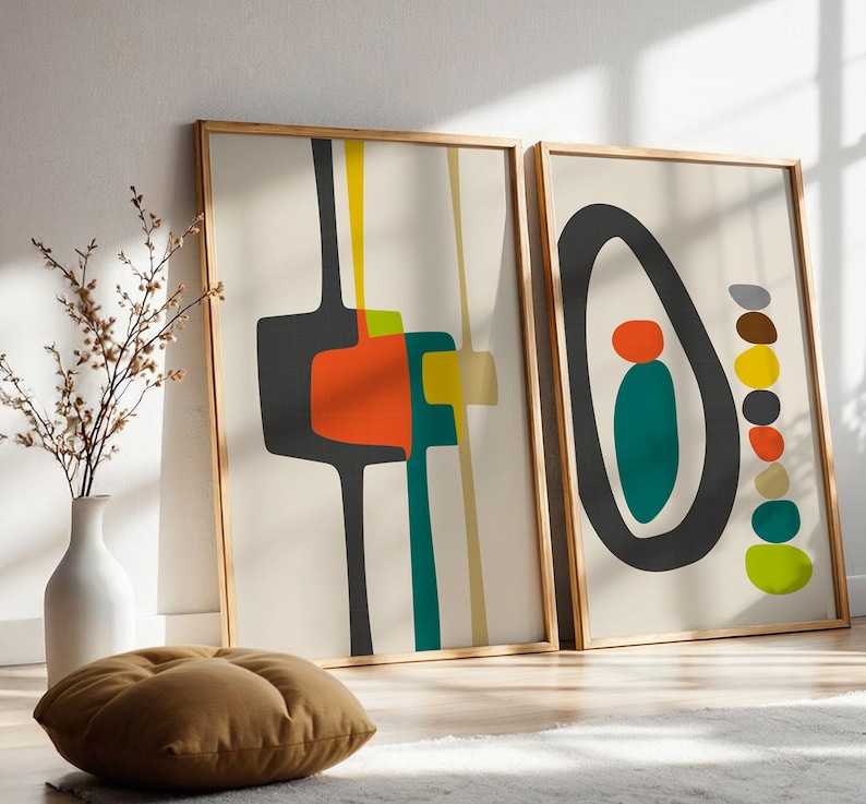 May include: Two framed rectangular wall art prints featuring abstract shapes in charcoal, orange, yellow, and teal on a cream background. The left print displays geometric lines and blocks, while the right print shows a large oval with stacked circles.