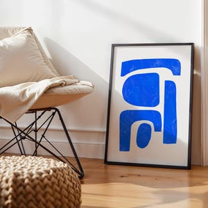 May include: A framed rectangular wall art print featuring bold, vibrant blue abstract shapes on a plain white background. The artwork is enclosed in a thin black frame, displaying organic, hand-painted style forms with visible brushstroke textures.