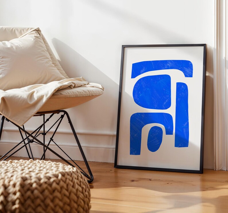May include: A framed rectangular wall art print featuring bold, vibrant blue abstract shapes on a plain white background. The artwork is enclosed in a thin black frame, displaying organic, hand-painted style forms with visible brushstroke textures.