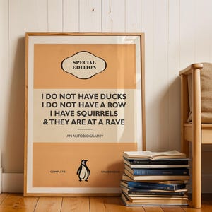 May include: A rectangular framed poster with a light orange and cream background featuring the text: SPECIAL EDITION, I DO NOT HAVE DUCKS, I DO NOT HAVE A ROW, I HAVE SQUIRRELS & THEY ARE AT A RAVE, AN AUTOBIOGRAPHY, COMPLETE, UNABRIDGED, and a penguin icon.