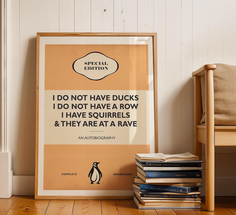 May include: A rectangular framed poster with a light orange and cream background featuring the text: SPECIAL EDITION, I DO NOT HAVE DUCKS, I DO NOT HAVE A ROW, I HAVE SQUIRRELS & THEY ARE AT A RAVE, AN AUTOBIOGRAPHY, COMPLETE, UNABRIDGED, and a penguin icon.