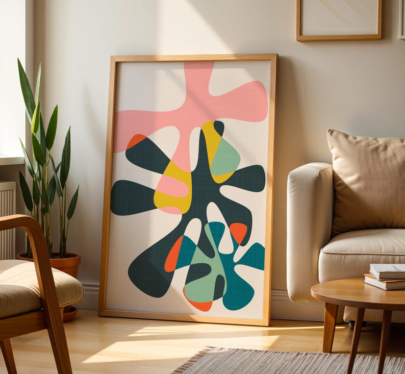 May include: A rectangular framed wall art piece featuring an abstract composition of organic, fluid shapes in shades of dark green, light pink, yellow, teal, and orange against a cream-colored background, enclosed in a light wood frame.