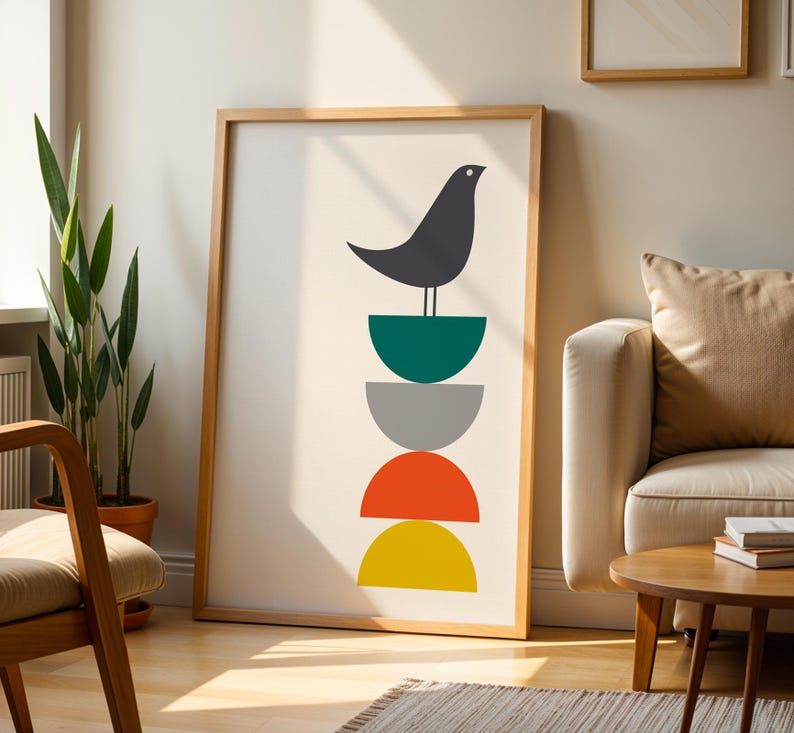 May include: A framed wall art print featuring a dark gray bird perched atop a vertical stack of four semi-circles in teal, gray, orange, and yellow. The artwork is set against a plain white background within a light-toned wooden frame.