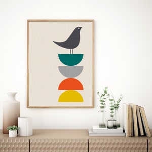 May include: A framed wall art print featuring a dark gray bird perched atop a vertical stack of four semi-circles in teal, gray, orange, and yellow. The artwork is set against a light beige background with a subtle, fine-textured linen appearance.