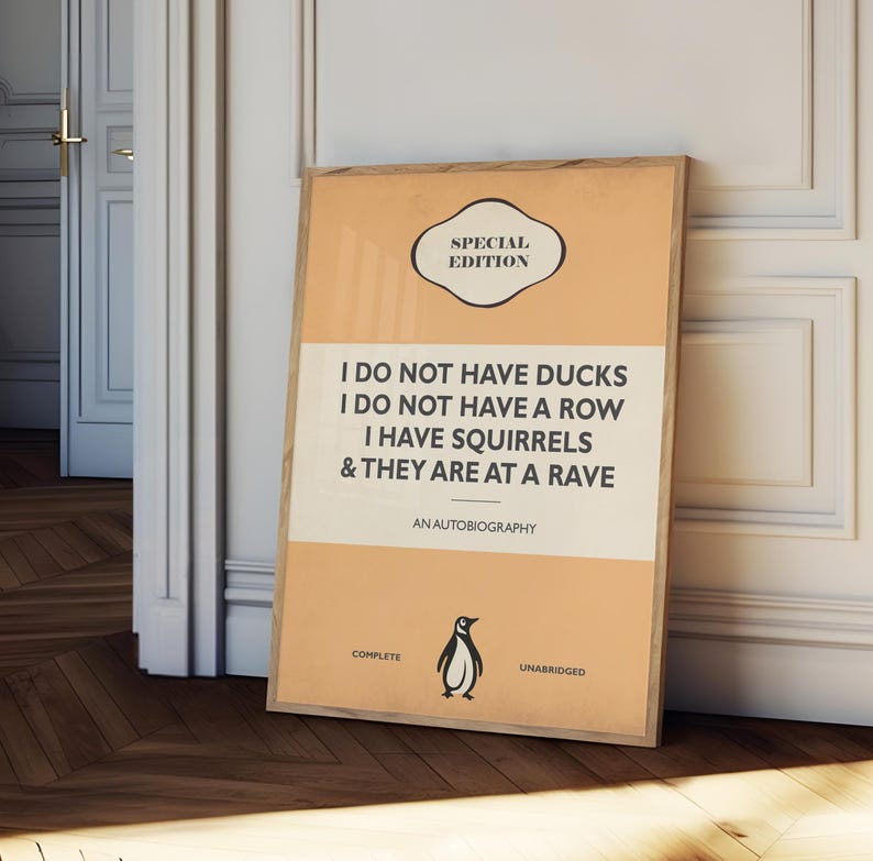 May include: A rectangular framed poster with a light orange background and a central cream-colored horizontal band. The text reads: SPECIAL EDITION, I DO NOT HAVE DUCKS I DO NOT HAVE A ROW I HAVE SQUIRRELS & THEY ARE AT A RAVE, AN AUTOBIOGRAPHY, COMPLETE, UNABRIDGED, with a small black penguin illustration.