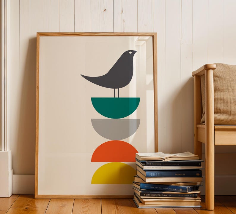 May include: A framed wall art print featuring a dark gray bird perched atop a vertical stack of four semi-circles in teal, light gray, orange, and yellow. The artwork is set against a cream background and enclosed in a light wood frame.