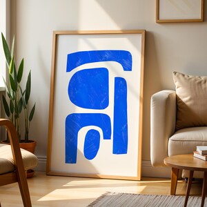 May include: A framed wall art print featuring abstract blue shapes on a white background. The artwork consists of several bold, interconnected blue forms with visible brushstroke textures, enclosed within a light-colored wooden frame.