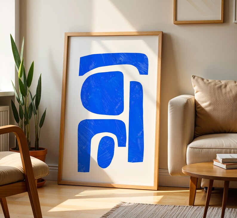 May include: A framed wall art print featuring abstract blue shapes on a white background. The artwork consists of several bold, interconnected blue forms with visible brushstroke textures, enclosed within a light-colored wooden frame.