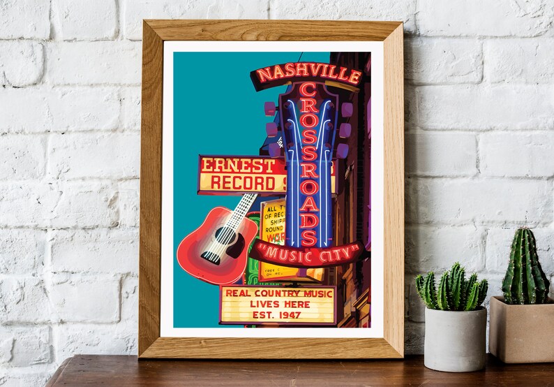 May include: A framed print featuring a vibrant illustration of a Nashville music scene. The artwork showcases a red guitar, neon signs reading "Nashville Crossroads Music City," and "Ernest Record," with the text "Real Country Music Lives Here Est. 1947."