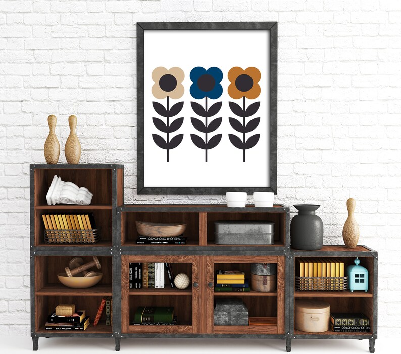 Op de afbeelding: Een ingelijst afdruk van drie gestileerde bloemen met bruine, blauwe en gele bloemblaadjes. De bloemen staan op een witte achtergrond en het frame is zwart. De afdruk staat op een houten plank met andere decoratieve items.