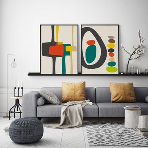 May include: Two framed wall art prints featuring abstract geometric shapes in charcoal, orange, teal, yellow, and beige. The left print displays interconnected block forms, while the right print shows a large oval enclosing a stack of colorful pebbles.