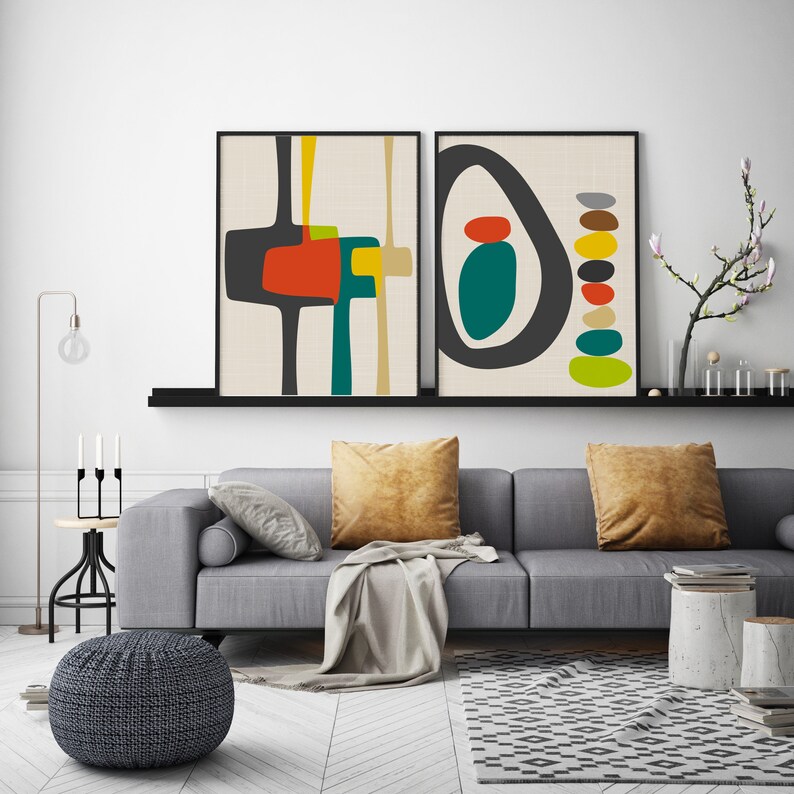 May include: Two framed wall art prints featuring abstract geometric shapes in charcoal, orange, teal, yellow, and beige. The left print displays interconnected block forms, while the right print shows a large oval enclosing a stack of colorful pebbles.