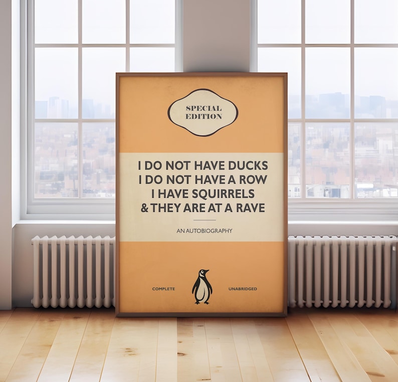 May include: A rectangular framed poster with an orange and cream background. The text reads: SPECIAL EDITION, I DO NOT HAVE DUCKS, I DO NOT HAVE A ROW, I HAVE SQUIRRELS, & THEY ARE AT A RAVE, AN AUTOBIOGRAPHY, COMPLETE, UNABRIDGED, with a penguin icon.